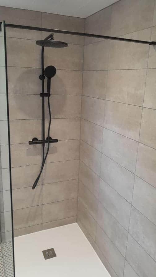 Détail de douche à l'italienne : colonne thermostatique noire, carrelage beige et receveur blanc