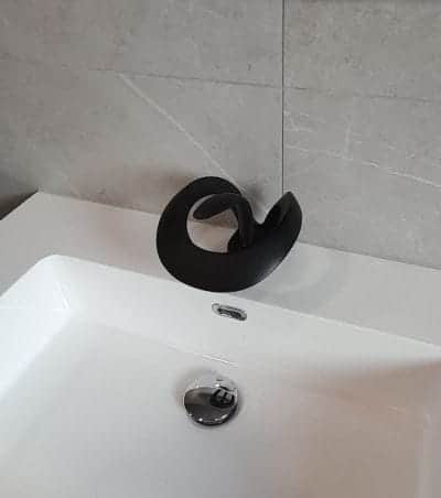 Mitigeur noir mat au design en volute installé sur une vasque blanche par AML Plomberie