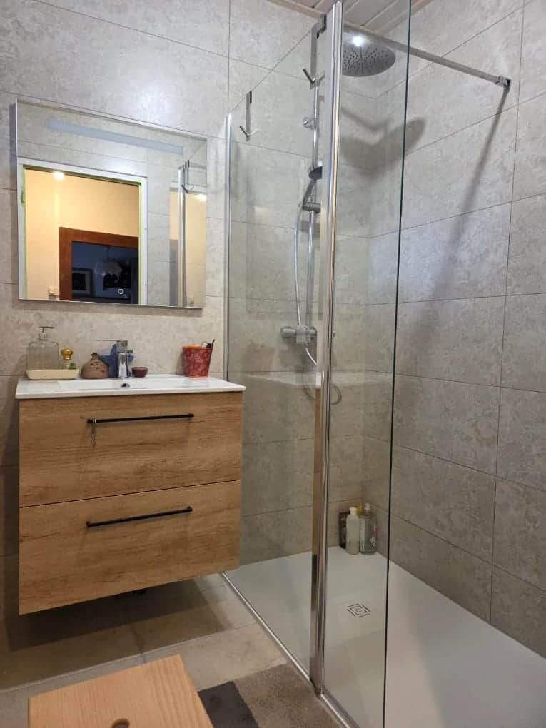 Salle de bain avec douche à paroi vitrée, carrelage beige et meuble vasque en bois, rénovée dans le Doubs